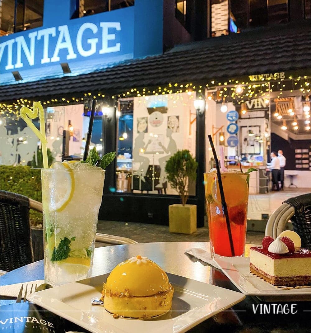 Deux boissons fraîches et deux desserts sur une table, le soir, devant la façade éclairée du Vintage